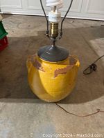 Full view of mustard yellow ceramic lamp base showing paint chipping and attached electrical socket with light bulb.