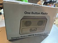 Box showing front label with 'One Button Radio' title and image of the radio, stating it is a simple retro AM/FM analogue radio.