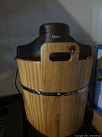 Front view of Oster 4-quart ice cream maker showing wooden bucket and black motor housing with Oster branding.