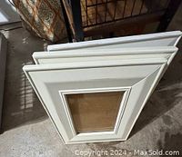 Three white and off-white picture frames stacked together, showing their layered and beveled edges.