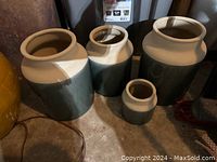 Photo showing four two-tone ceramic pots of various sizes on a concrete floor with neutral gray and brown tones.