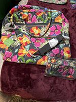 Full view of the Vera Bradley overnight travel bag and matching wallet set with bright colorful floral pattern on a dark background.