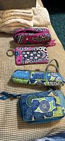 Photo showing two Vera Bradley sets on a beige background. Top set pink with floral and paisley pattern with zip-around wallet and small pouch. Bottom set blue/green with patchwork floral patterns featuring wallet and soft sunglass case.