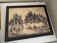 Framed painting depicting a city skyline with tall buildings and a suspension bridge over water. Features muted colors and impressionist style.