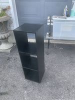 Front angle view of black narrow bookshelf with three enclosed compartments.