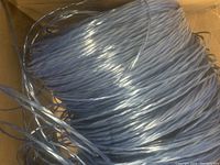 Top view of thick, shiny silver poly twine loosely coiled inside a cardboard box, showing texture and thickness of the twine fibers.