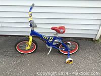 Side view of the blue and yellow Paw Patrol themed boy's bicycle featuring red seat and 14 inch wheels with training wheels. Missing pedals visible.
