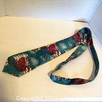 Christmas necktie laid out showing full length and festive design of Santa in sleigh on teal background.