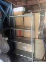 Full view of the grey heavy duty metal shelving showing four adjustable shelves in a storage space with surrounding boxes and items.