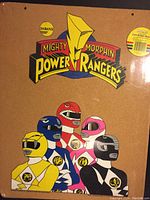 Front view of cork bulletin board featuring colorful Mighty Morphin Power Rangers logo and characters, covered in plastic wrap.
