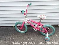 Full side view of the pink and green girl's bicycle with training wheels showing floral seat and handlebar bell.