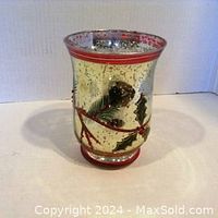 Front view of silver colored glass Christmas candle holder with holly design and red trim.