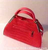 Front and side view of a sturdy hot pink handbag with a simulated crocodile texture and metal trim on the handles.