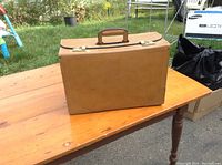Front view of tan leather briefcase on wooden table outdoors showing full case and handle.
