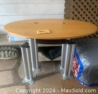 Oval light pine desk surface with metal legs detached, screws placed on top, showing smooth oval tabletop with light wood grain.