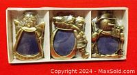 Set of three brass Christmas ornaments in original packaging showing angel, Santa, and snowman with blue picture frames inside a box.