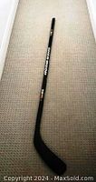 Photo shows full length of black Sherwood 19K wood hockey stick lying on a beige carpet, fully visible with graphics.