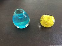 Two glass paperweights on a dark surface, blue and yellow colors visible with bubble inclusions