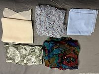 Five ladies neck scarves displayed folded on a dark surface showing variety in colors and fabrics