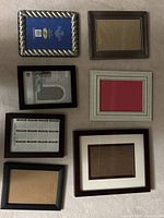 Photo showing 7 assorted picture frames arranged on flat surface with a variety of shapes, sizes, and materials visible.