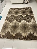 Photo of laid out beige and brown geometric patterned area rug on white tiled floor, showing overall design and size.