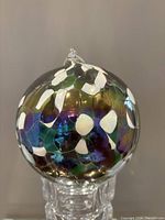 Close-up front view of the multi-colored art glass orb ornament with iridescent finish and white petal-like patterns.