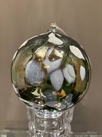 Front view of the multicoloured art glass orb ornament showing iridescent surface and hanging loop on top.