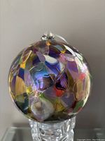 Front side view of the blown glass orb showing multi-colored abstract pattern and clear hanging loop on top
