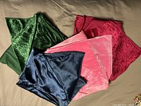 Four folded velvet/velour fabric pieces in green, blue, pink, and burgundy colors on a surface.