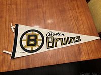 Full photo of the white felt Boston Bruins pennant with team logo and text.