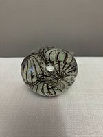 Clear glass paperweight with brown swirl pattern visible on top and side, placed on a flat surface.