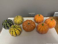 Eight plastic pumpkin decorations of varying colors and styles on a table, including one candle pumpkin and seven decorative pumpkins.