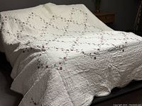 Ivory quilted double bedspread with burgundy floral pattern displayed on a bed