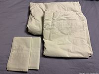 Four light green bedding items arranged on a surface: fitted sheet, flat sheet, and two pillowcases. Pillowcases show a subtle stitched pattern near the open edge.