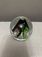 Clear glass spherical paperweight with internal red and green colored swirls visible against grey background, viewed from front angle.