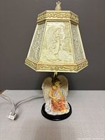 Photo of small lampshade with detailed embossed angels and black base featuring seated angel figure, cords at side.