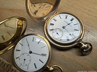 Two open-faced pocket watches showing dials and cases