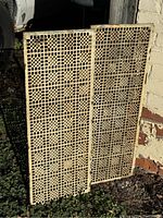 Single grate leaning outdoors against brick wall, front view showing cream painted lattice pattern