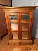 Front view of the wooden medicine cabinet showing two doors with textured glass and wooden slats. Two small drawers at the bottom with wooden knobs.