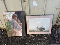 Photo of two framed artworks leaning against a container outdoors, showing both the oil painting of a woman and the boat print.
