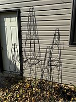 Front view of four black metal trellises of various heights leaning against exterior siding.