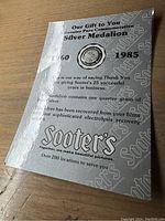 Paper sleeve covering the silver medallion, detailing the anniversary from 1960 to 1985 and silver recovery process.