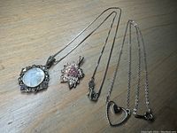 Full view of two silver pendants with their silver chains laid flat on wood surface.