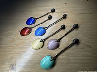 Full set of six sterling silver spoons with colorful enamel leaf-shaped bowls, laid out on wooden surface.