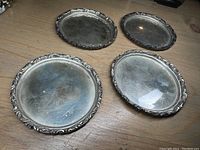Four oval sterling silver coasters with decorative rim on wooden surface
