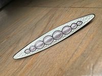 Side angle showing texture, enamel ovals, and shape of the brooch on a wood surface