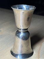 Side view showing full height and shape of shiny sterling silver jigger with minor dents.