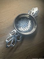 Top view showing round perforated bowl and ornate pierced handles of sterling silver tea strainer.