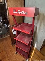 Front view of the red metal Tim Hortons display rack showing four angled shelves and top plastic header with logo.