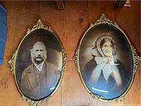 Full view of both Victorian portraits, showing oval shape, metal frames, convex glass, and condition.